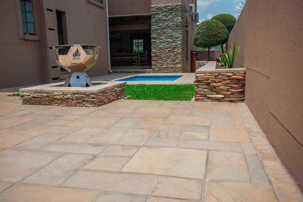 Natural stone outdoor living space with fire pit, rought textured paving patio and pool