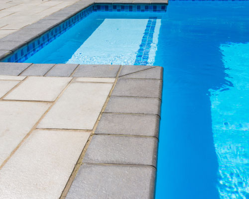 Smooth and dark coping used around a pool with matching contrasting lighter pavers